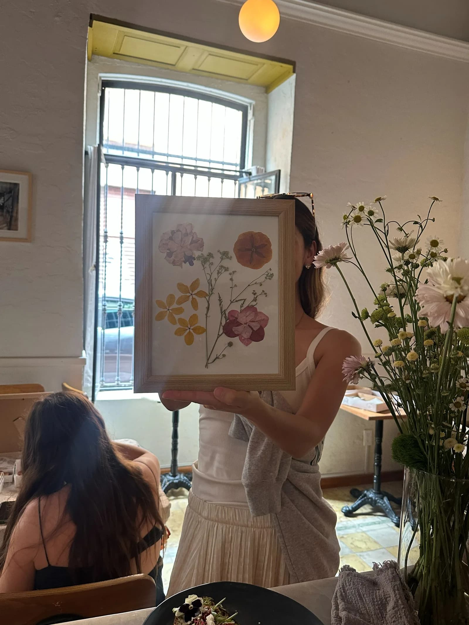 Una alumna sostiene su composición de flores prensadas junto a la ventana.